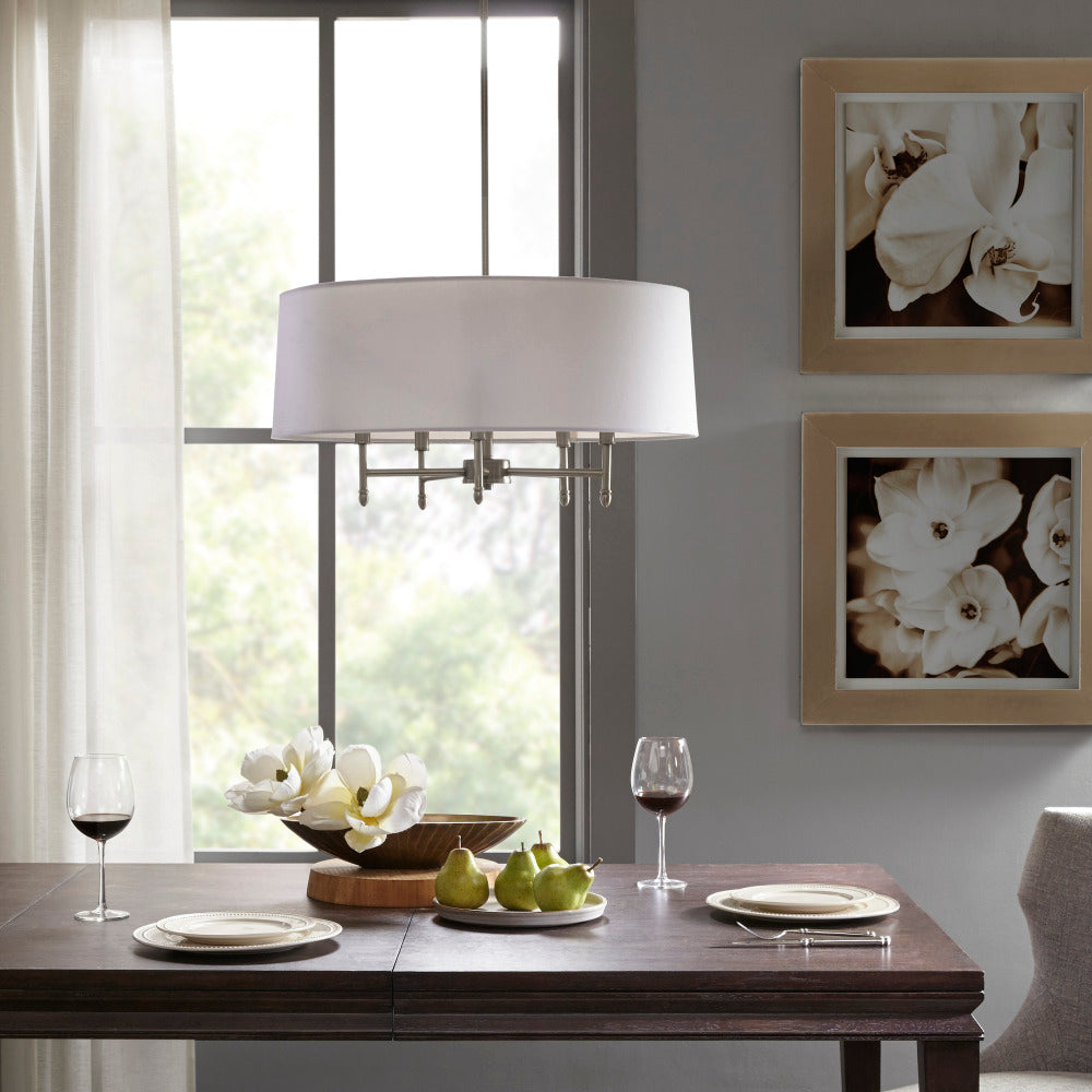 5-light drum shade chandelier with white cotton-linen shade and silver plated brass frame, hanging over dark wood dining table with plates, wine glasses, and floral centerpiece.