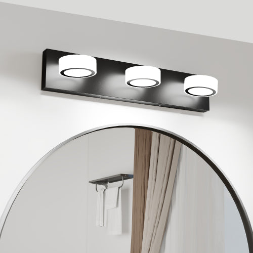 Matte black 3-light LED vanity light with white acrylic shades, mounted above a round mirror in a bathroom, offering bright 6000K lighting.