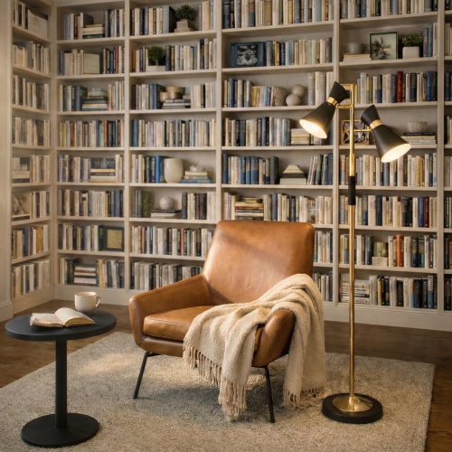 Double spot floor lamp with brushed gold finish and metal base, 4-way switch, illuminating a library reading nook with a leather armchair and bookshelves.