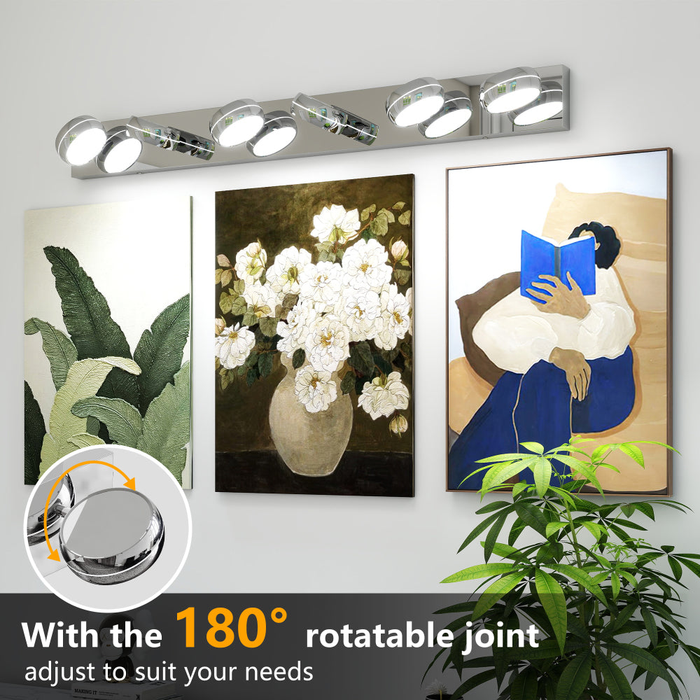 Modern chrome LED vanity light bar with 180° rotatable joints, mounted above mirror with framed artworks and greenery