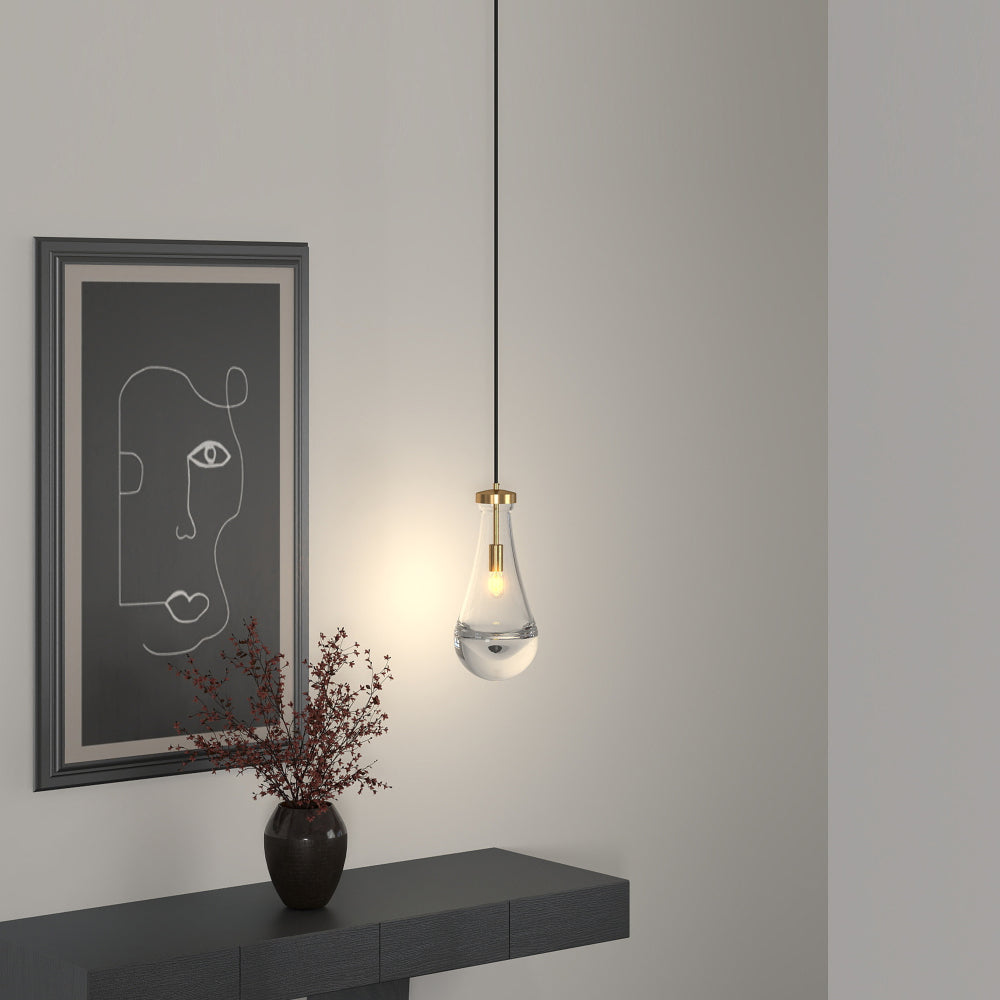 Single Raindrop Pendant Light with hand-blown clear glass shade and brass accents, illuminating an entryway with a console table, vase of red branches, and abstract wall art.