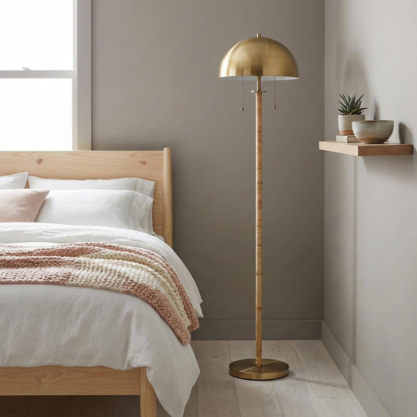 2-light floor lamp with gold brass dome shade and natural rattan tube stem, dual pull chains, standing beside a bed in a well-lit bedroom.