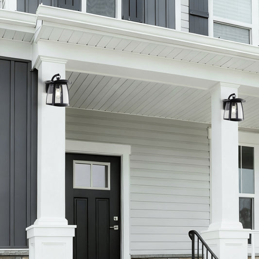 Two black solar wall lanterns with clear glass panels installed on white porch columns, illuminating a modern home entrance with black door