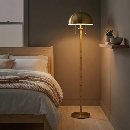 2-light floor lamp with gold brass dome shade and natural rattan tube stem, dual pull chains, placed beside a bed in a softly lit bedroom.