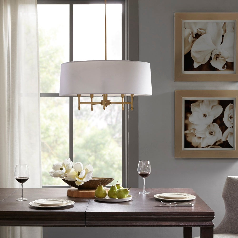 5-light drum shade chandelier with white cotton-linen shade and gold plated brass frame, hanging over dark wood dining table with plates, wine glasses, and floral centerpiece.