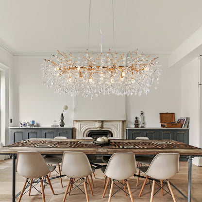 Gold Tree Branch Crystal Chandelier with gold branches and hanging crystal drops, illuminating a modern dining room with wooden table and fireplace.