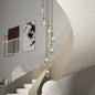 Gold 7-light raindrop cluster pendant chandelier hanging in a modern stairwell with curved walls and abstract art