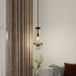 Raindrop Pendant Light featuring hand-blown clear glass shade and black rod, illuminated near brown curtains in a living room.