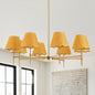 Gold Boho Rattan Chandelier with 8 yellow rattan lampshades hanging in a bright room with large windows and a textured brick wall.