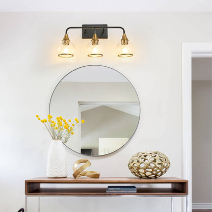 Black & gold industrial 3-light vanity wall sconce with clear glass shades above a round mirror in a living space with console table and yellow floral decor.