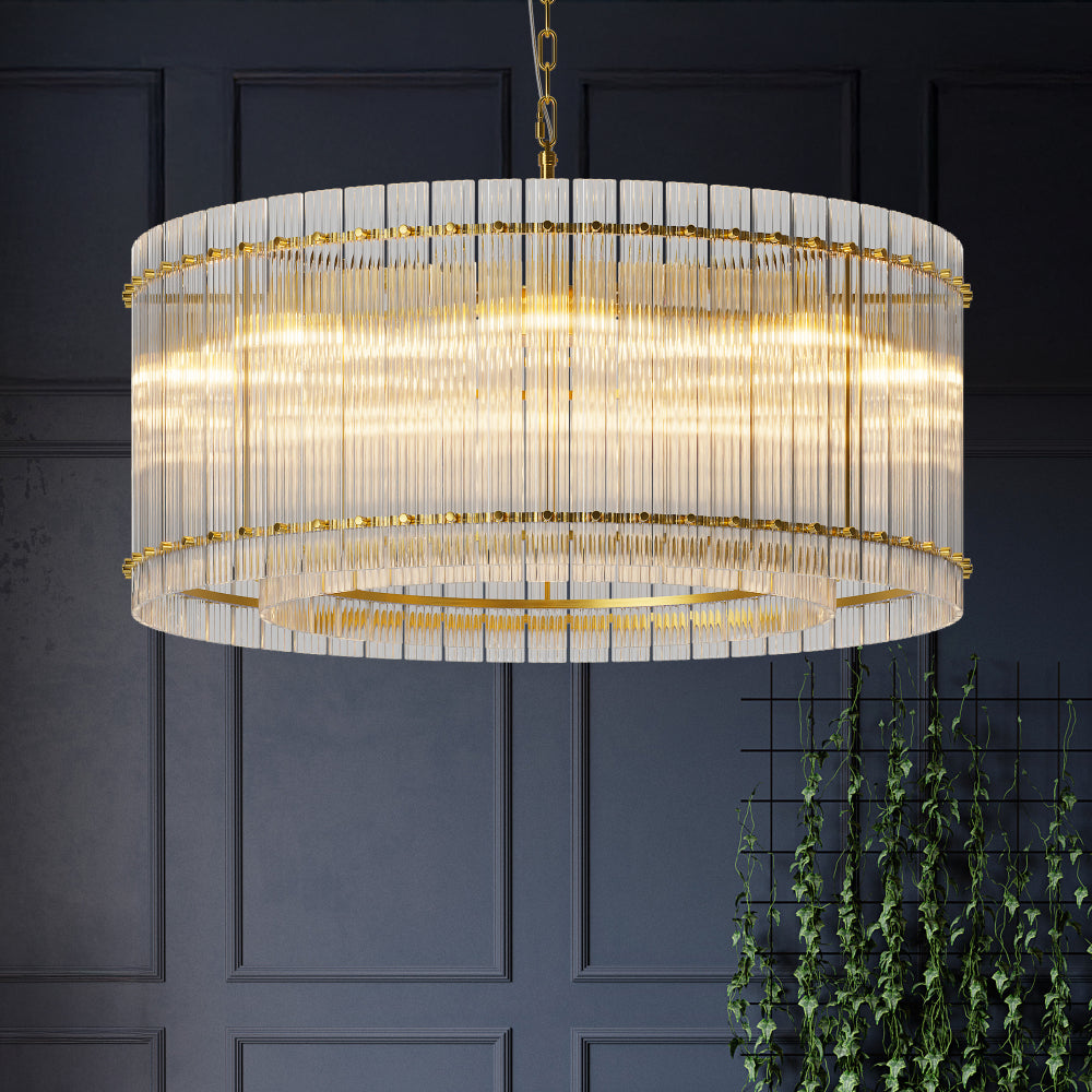 Round Water Ripple Crystal Glass Chandelier with gold trim, illuminated and hanging in a room with dark walls and green plants.