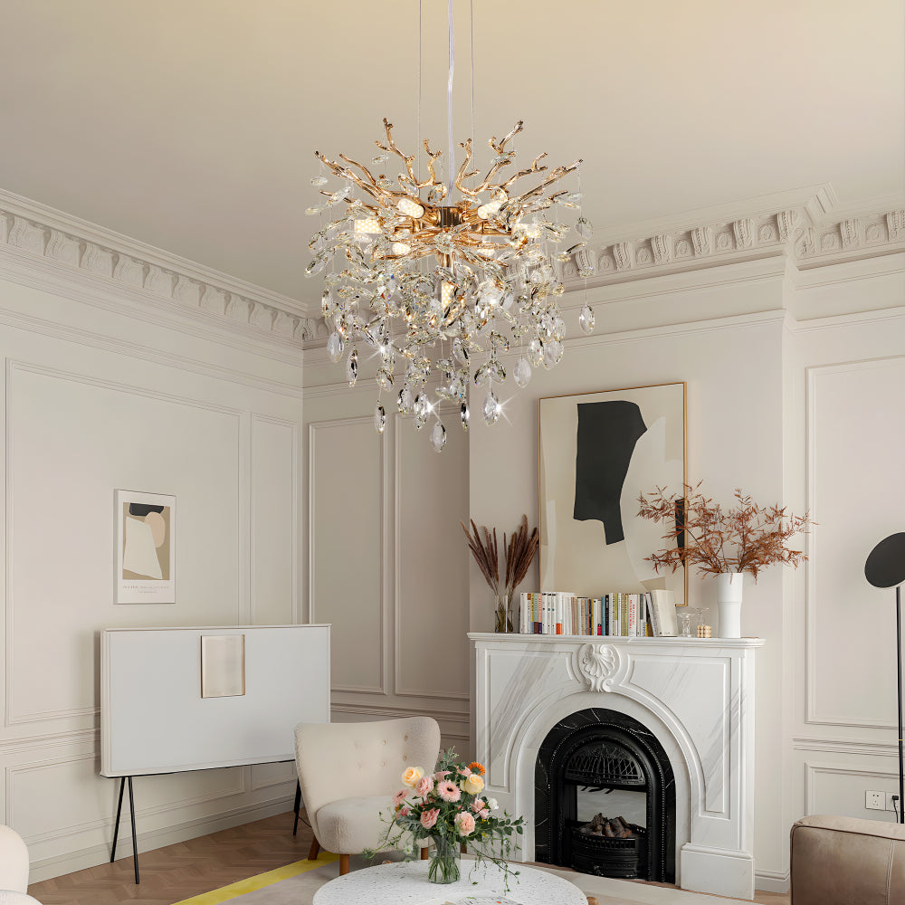 Gold tree branch crystal chandelier with crystal accents in a living room featuring white paneled walls and a marble fireplace.
