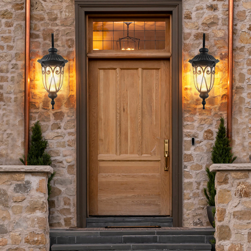 Pair of black vintage outdoor wall lanterns flanking wooden entry door on stone wall, illuminated to enhance exterior ambiance.