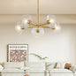 5-light gold mid-century modern sputnik chandelier with clear glass shades in a living room with a beige sofa and Keith Haring artwork.