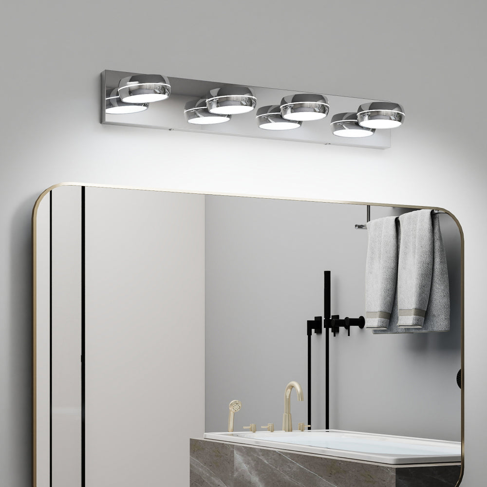 Modern chrome 4-light LED vanity light bar, 28 inches, mounted above a gold-framed bathroom mirror with towels and fixtures below