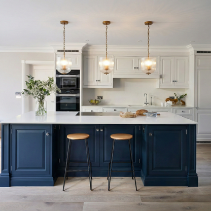 Three coarse gold metal pendant lamps with clear glass shades hanging over a kitchen island with white upper cabinets and blue lower cabinets.