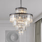 23.6-inch 5-tier K9 crystal chandelier with 15 lights, black frame, hanging in a modern living room with white walls, a circular mirror, and curtains.
