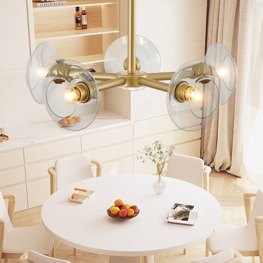 Gold mid-century modern sputnik chandelier with clear glass shades above a kitchen dining table with white cabinets and a fruit bowl.