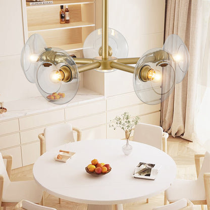 Gold mid-century modern sputnik chandelier with clear glass shades above a kitchen dining table with white cabinets and a fruit bowl.