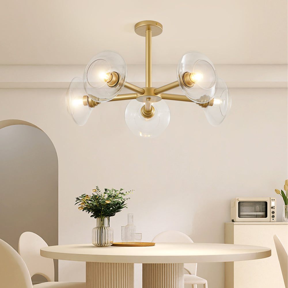 Gold mid-century modern sputnik chandelier with clear glass shades hanging over a dining table with greenery and minimalist decor.