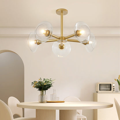 Gold mid-century modern sputnik chandelier with clear glass shades hanging over a dining table with greenery and minimalist decor.
