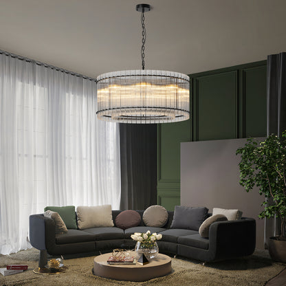 Modern round crystal glass chandelier with warm light, hanging in a living room with dark gray sectional sofa, green walls, and white curtains.