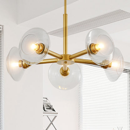 Illuminated gold sputnik chandelier with clear glass shades glowing warmly in a modern room with white walls and window blinds