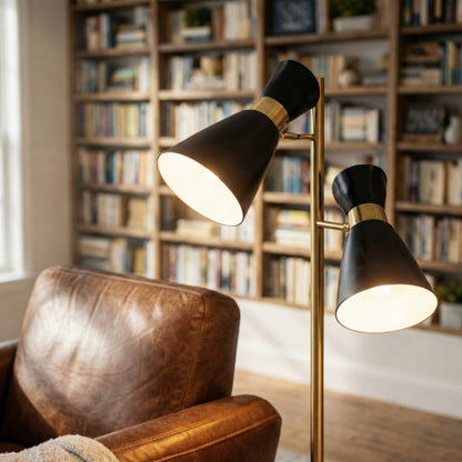 Modern double spot floor lamp with brushed gold metal base and black adjustable shades, providing reading and accent lighting in a cozy living space with bookshelves.