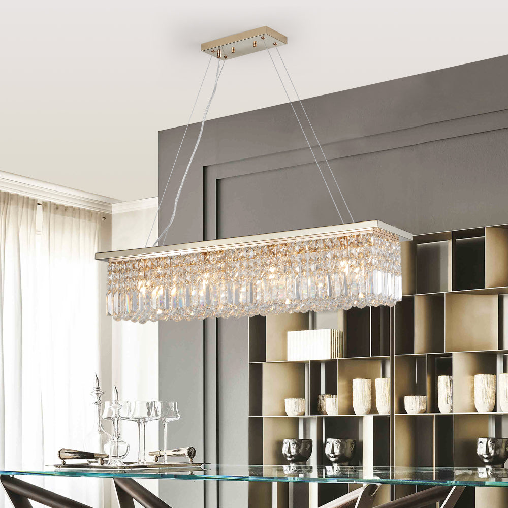 39.4-inch rectangle crystal raindrop chandelier with gold finish, 8-light modern pendant for dining room or kitchen island, hanging over a glass dining table with dark chairs and gray wall shelves.