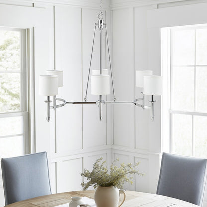 Bedford Collection 6-light chandelier with chrome curved frame and white drum shades hanging over a dining table in a bright room with windows.