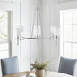 Bedford Collection 6-light chandelier with chrome curved frame and white drum shades hanging over a dining table in a bright room with windows.
