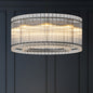 Close-up of modern round black crystal glass chandelier with warm illumination, showcasing layered glass rods against a dark wall.