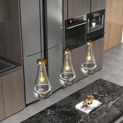 Three Raindrop Pendant Lights with hand-blown clear glass shades and brass accents, above a black marble kitchen island with geometric decor.