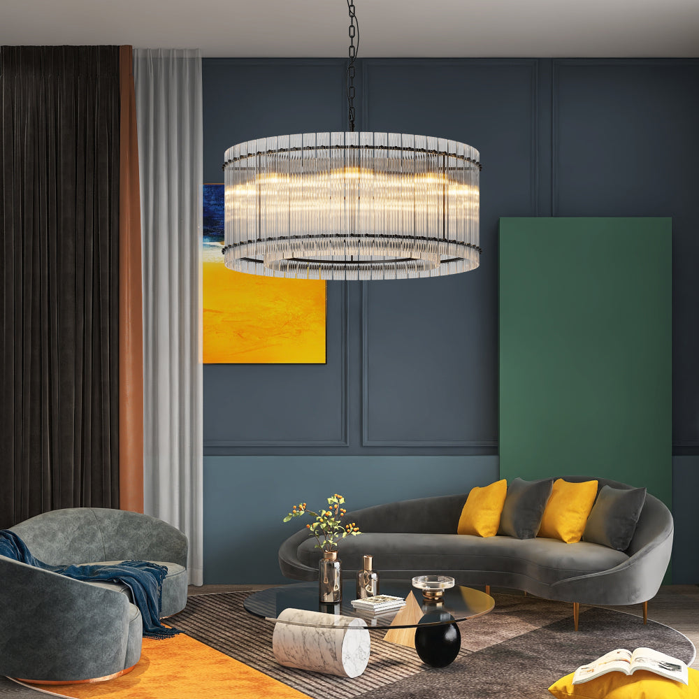 Modern round crystal glass chandelier with warm light, in a living room with dark blue walls, gray curved sofa with yellow pillows, and glass coffee table.