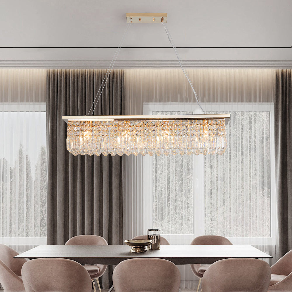 39.4-inch rectangle crystal raindrop chandelier with gold finish, 8-light modern pendant for dining room or kitchen island, hanging over a dark dining table with beige chairs and gray curtains.